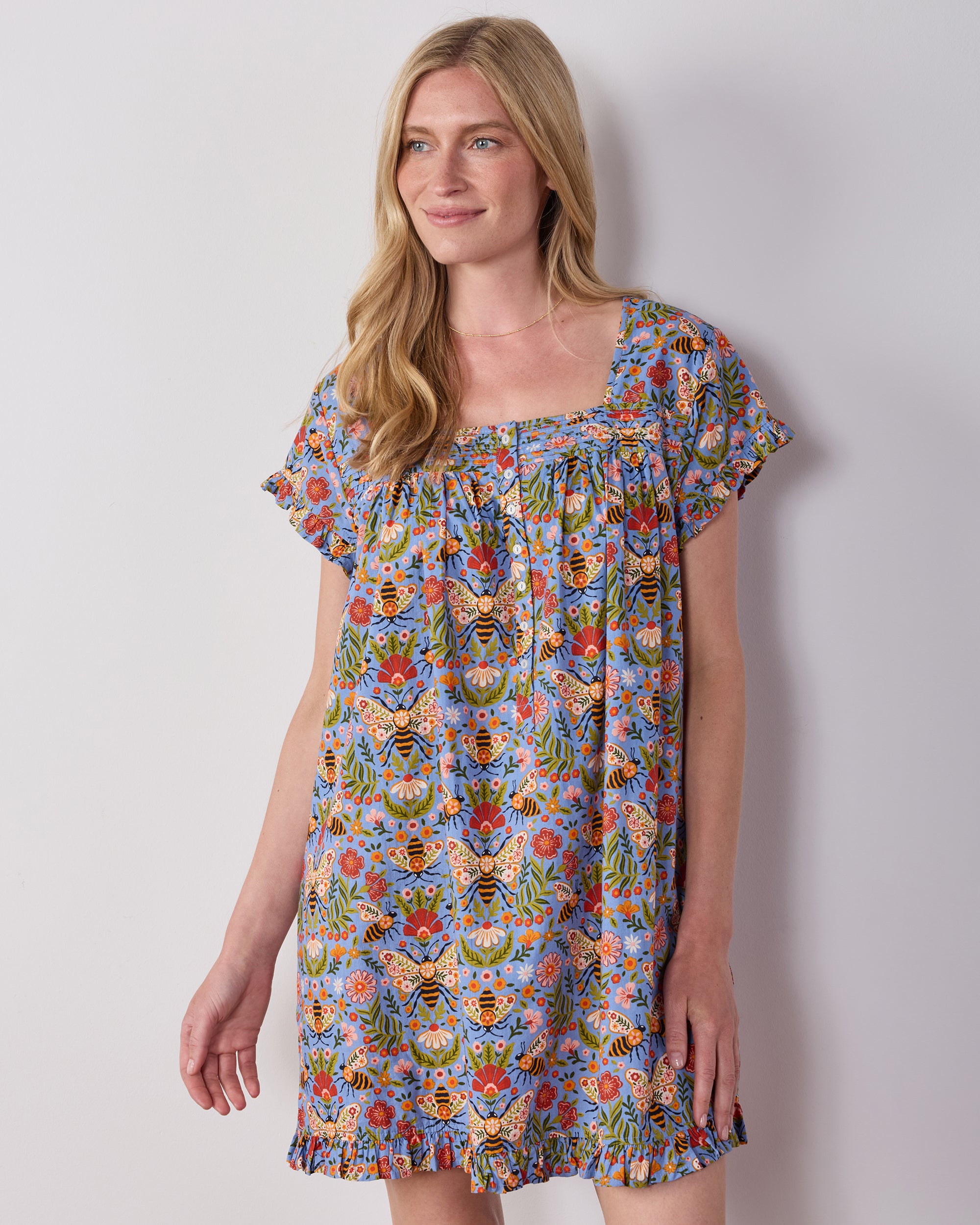 Person wearing the Delphinium Blue Bee Tapestry pintuck nightgown with short sleeves, a square neckline, and ruffled hem.