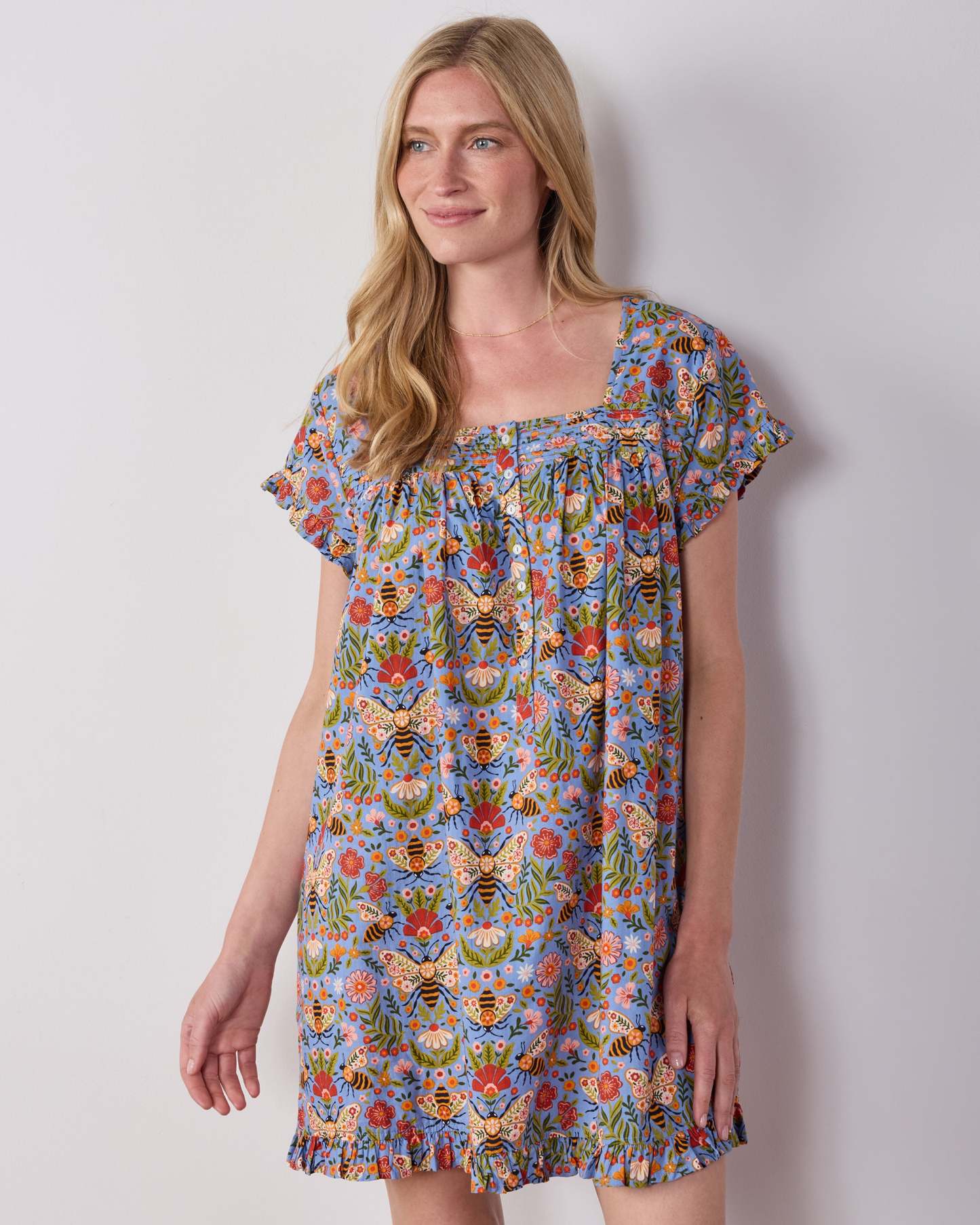 Person wearing the Delphinium Blue Bee Tapestry pintuck nightgown with short sleeves, a square neckline, and ruffled hem.