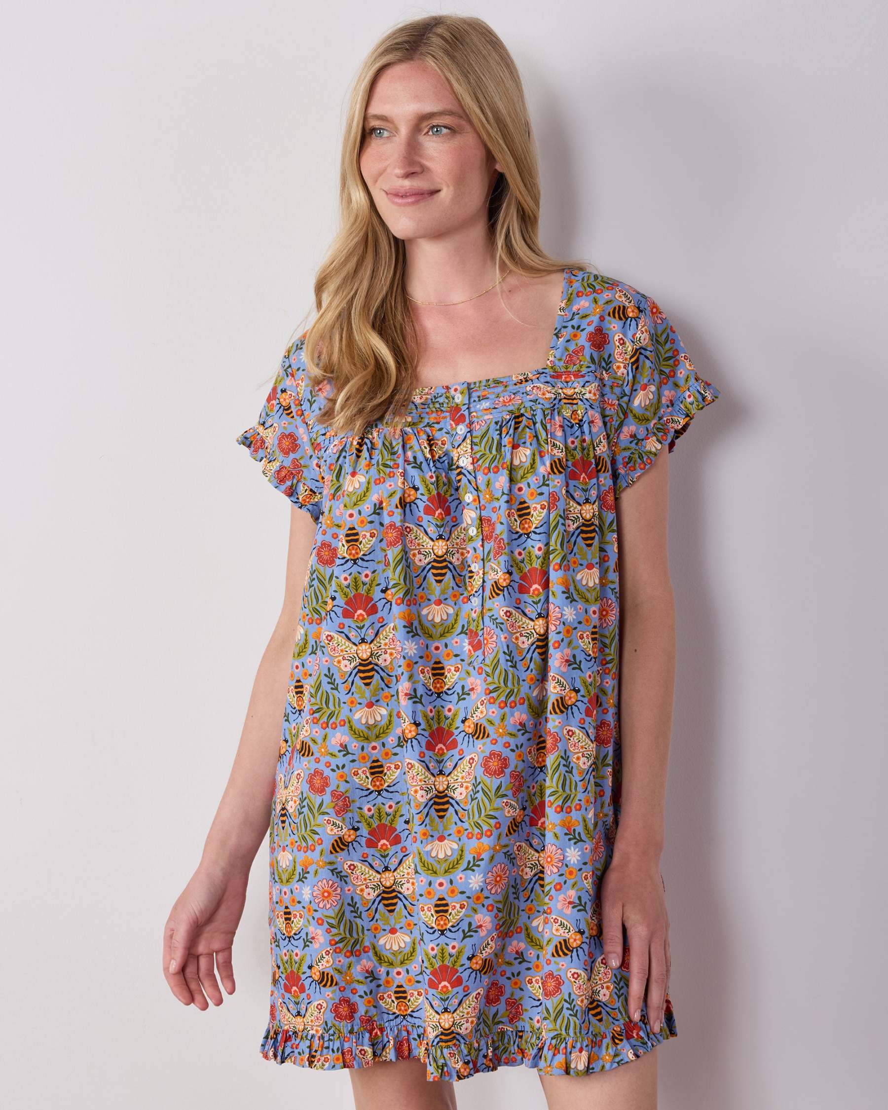 Person wearing the Delphinium Blue Bee Tapestry pintuck nightgown with short sleeves, a square neckline, and ruffled hem.