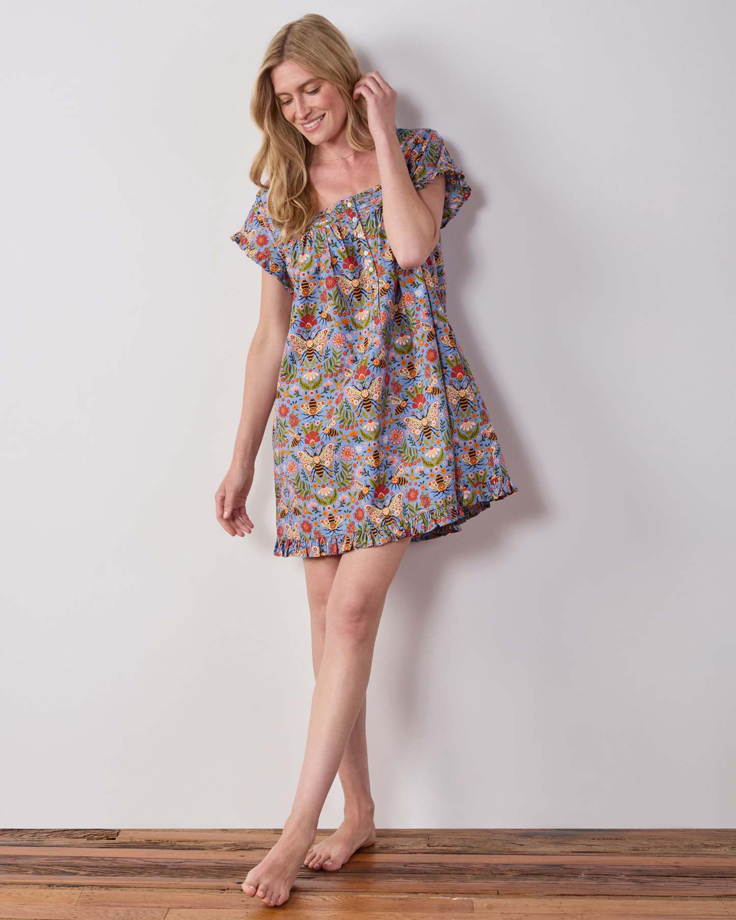 Model wearing the blue Bee Tapestry pintuck nightgown, shown at an angled view with its ruffled hem and short sleeves.