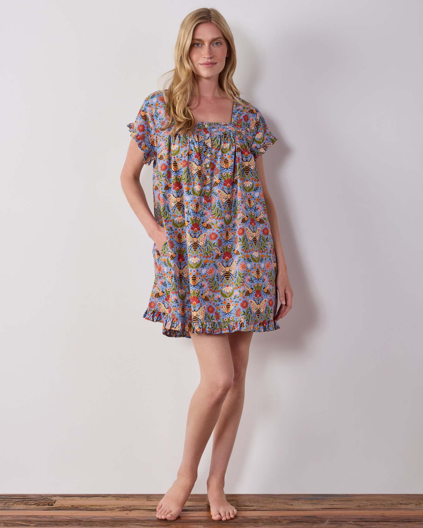 Model wearing the blue Bee Tapestry pintuck nightgown, shown from the front with short sleeves and a ruffled hem.