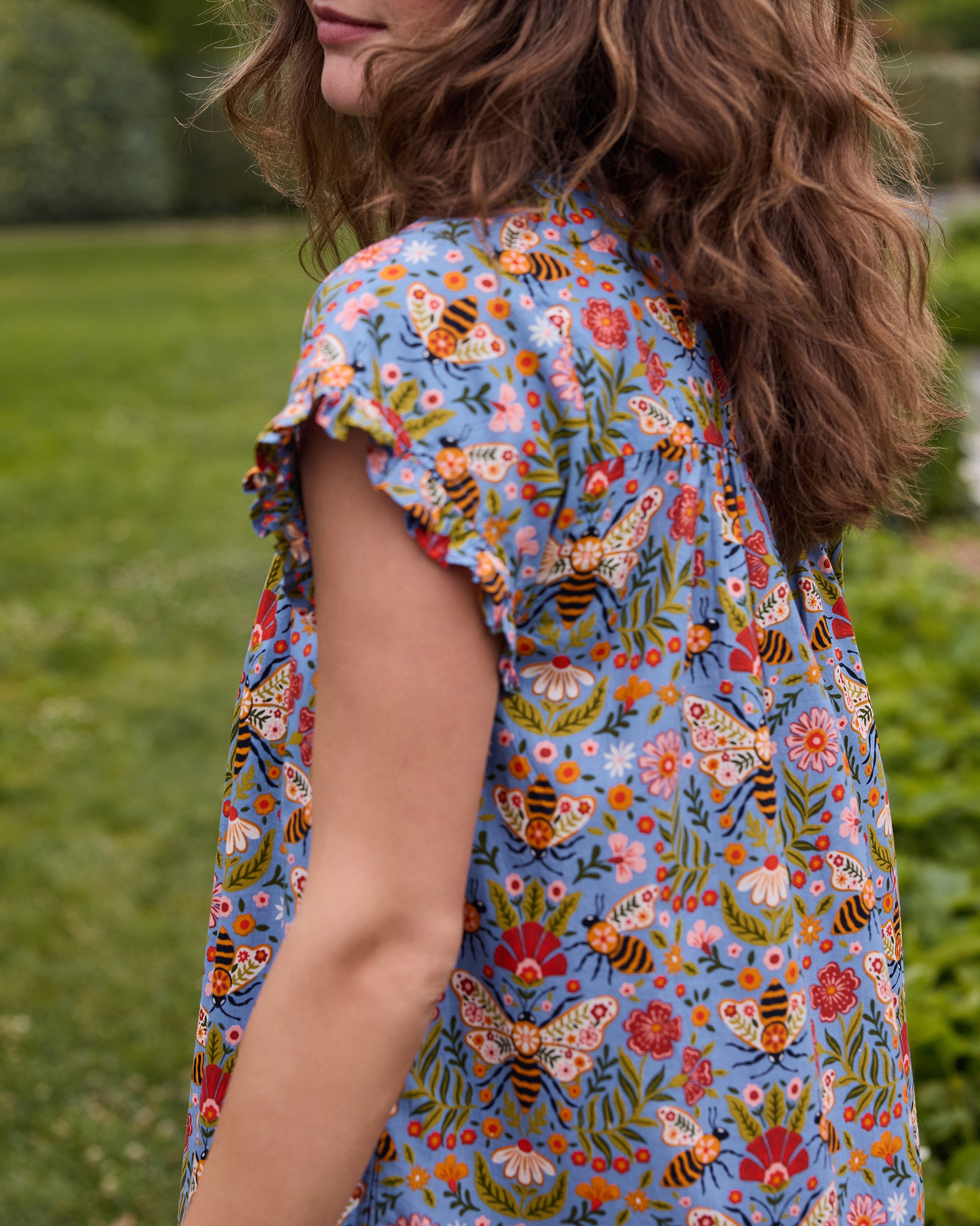 Close-up of a person wearing the Delphinium Blue Bee Tapestry floral-print pintuck nightgown, showing the ruffled sleeve and patterned fabric.