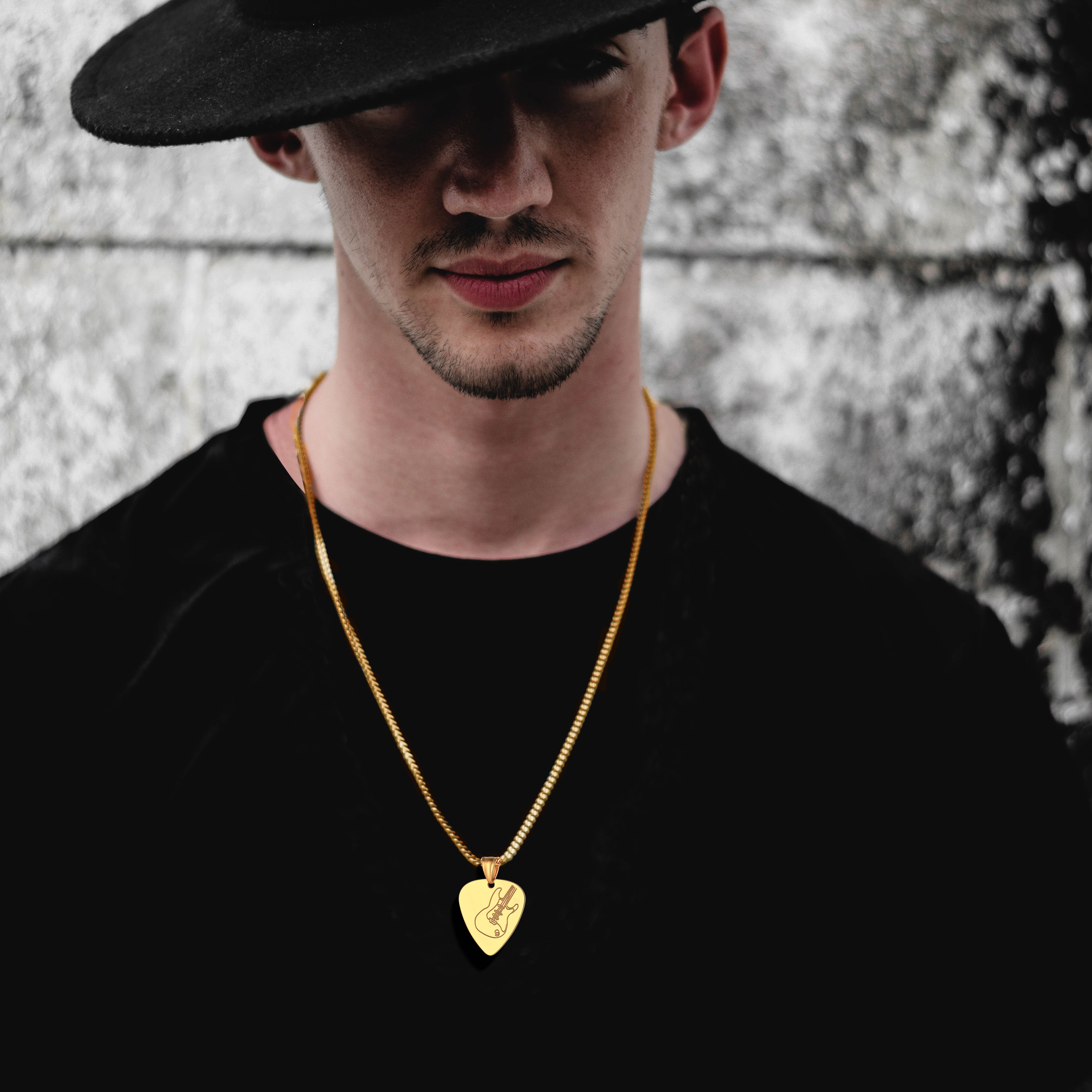 Man in black hat with gold guitar pick necklace on black t-shirt 