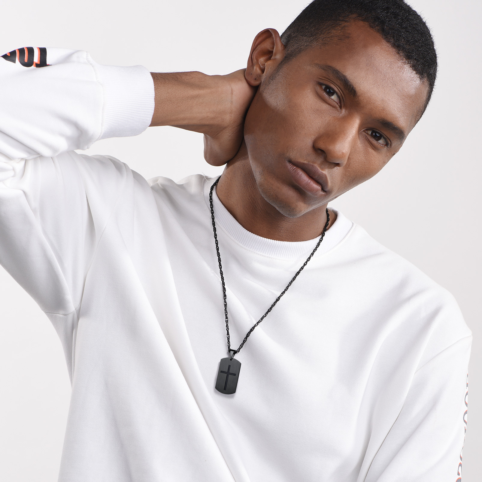 Black cross dog tag necklace worn by male model in white sweatshirt