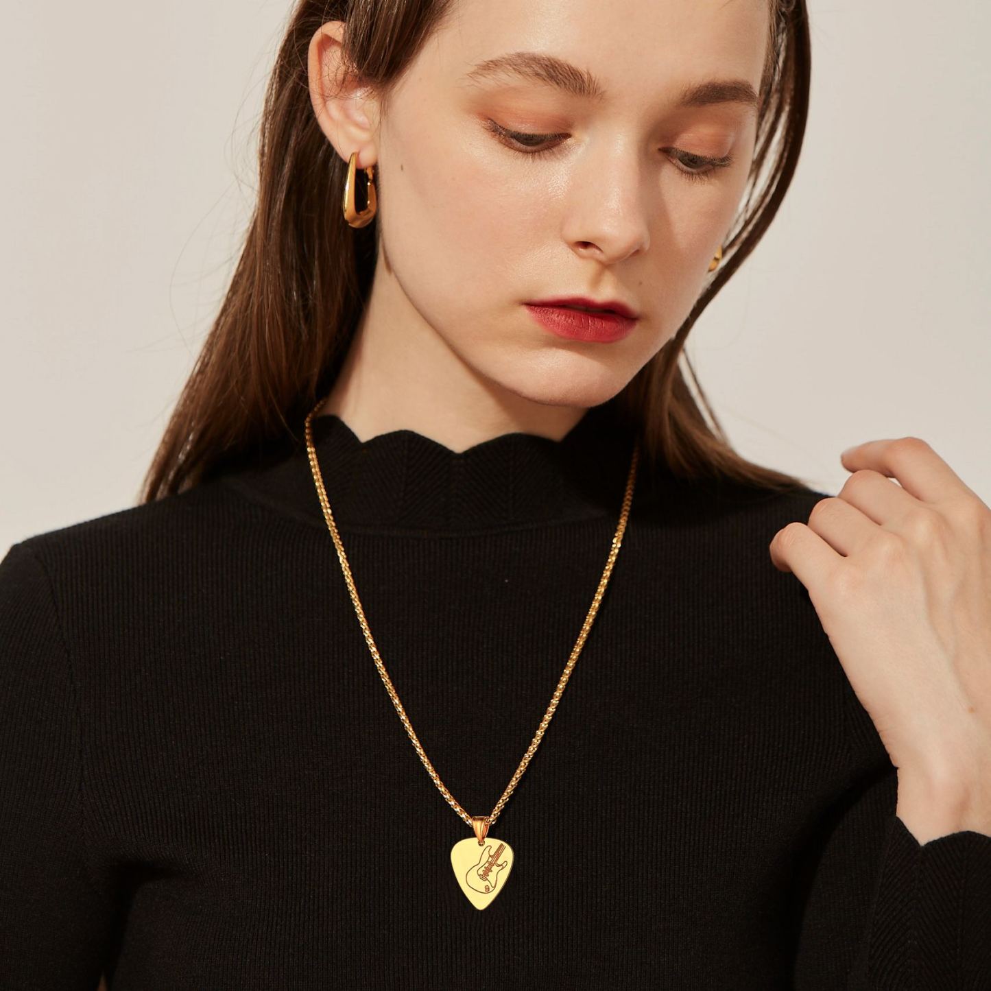 Woman in black top with gold guitar pick necklace and hoop earrings 