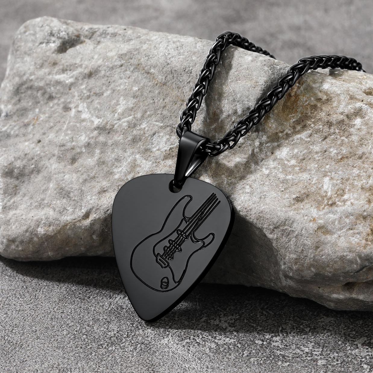 Black stainless steel guitar pick necklace on stone surface 