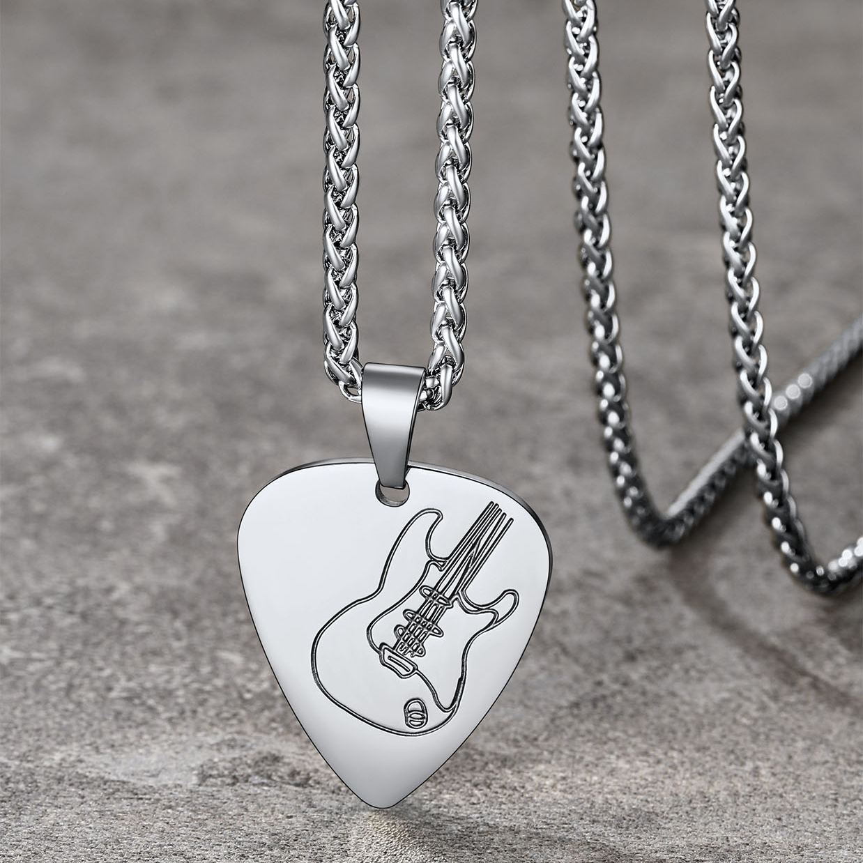 stainless steel guitar pick necklace on stone surface 