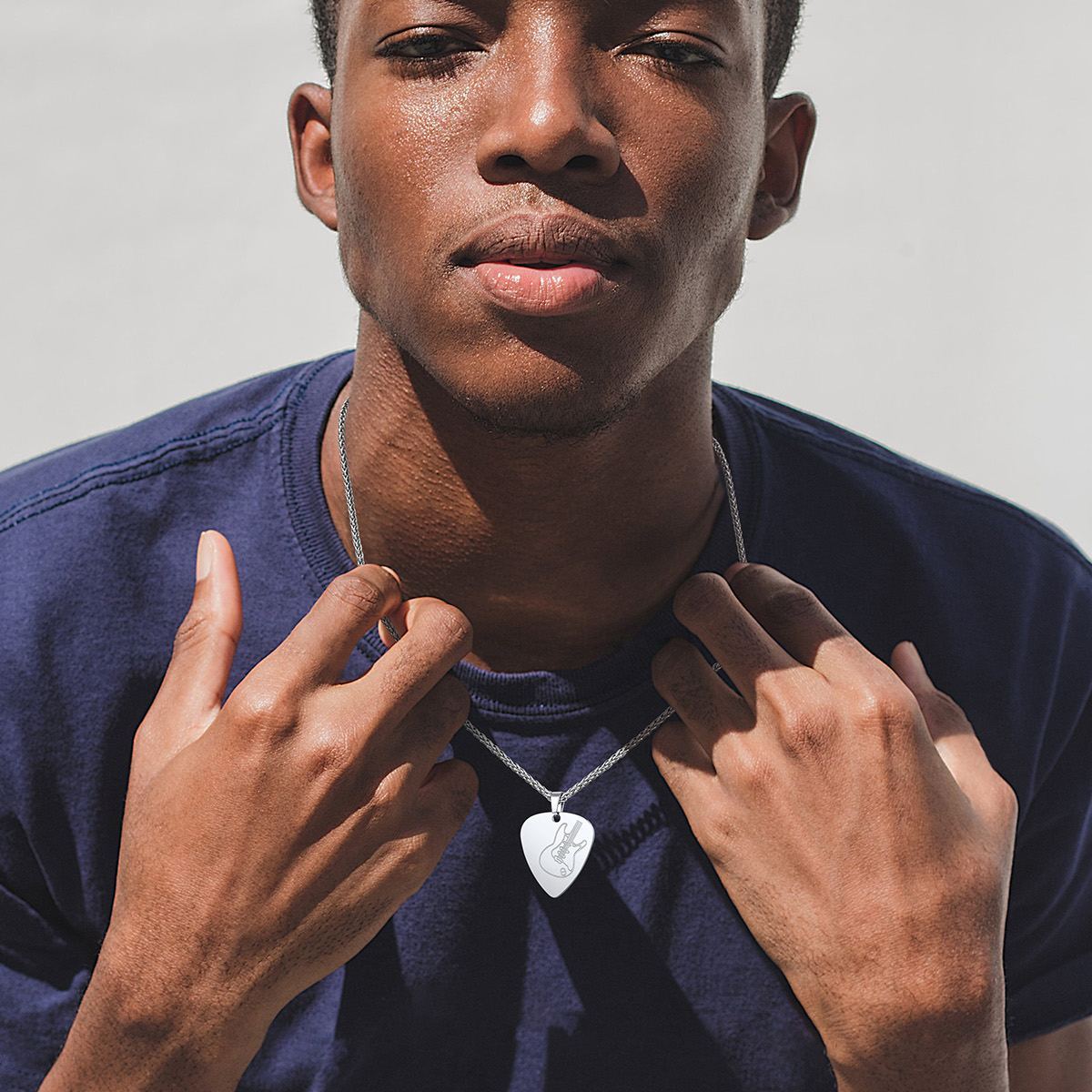 Man adjusting silver PROSTEEL guitar pick necklace on navy t-shirt 
