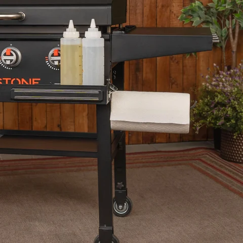 Lower right portion of the griddle shown displaying a paper towel roll on the holder and squeeze bottels in the front shelf tray