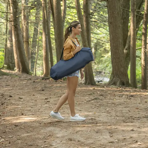 Young woman walking through wooded area, carrying bag over her shoulder.