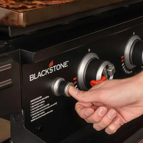 The electric push button ignition being pressed to start up the griddle