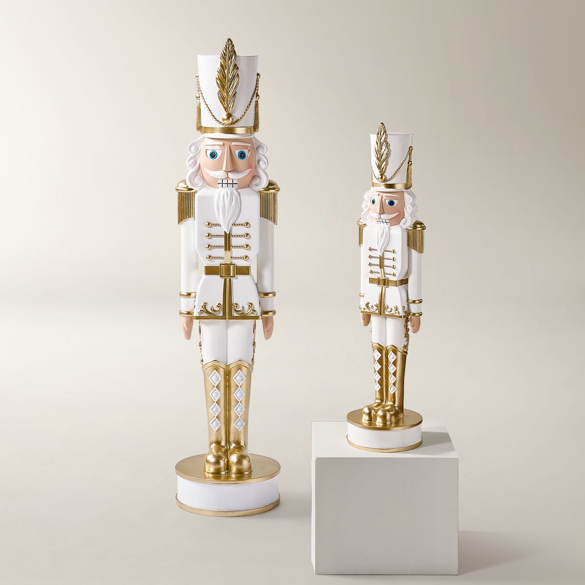 Pair of decorative white and gold standing holiday nutcrackers in two sizes displayed on a pedestal and neutral background.