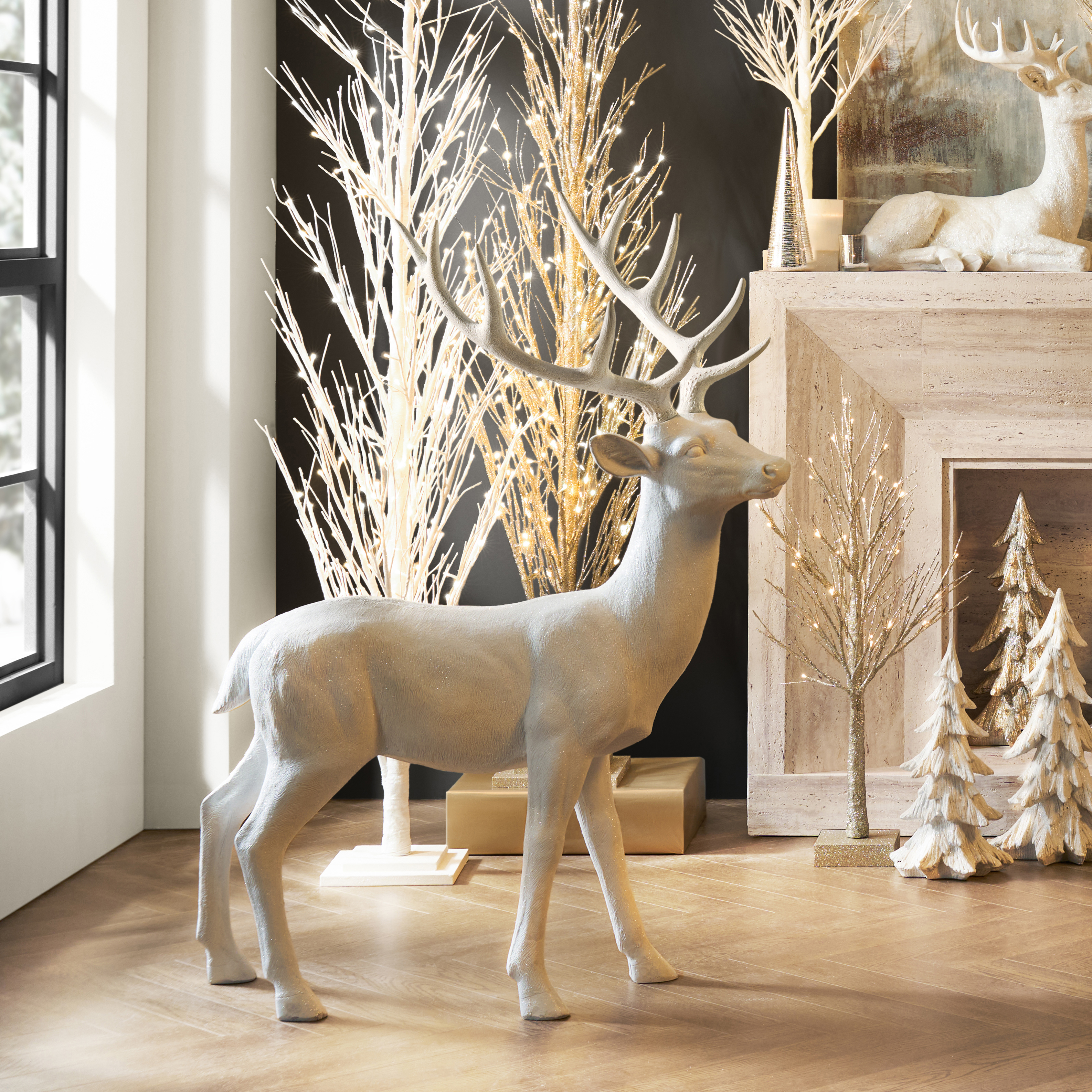 White reindeer statue styled with illuminated gold twig trees and metallic holiday accents in a modern living room.