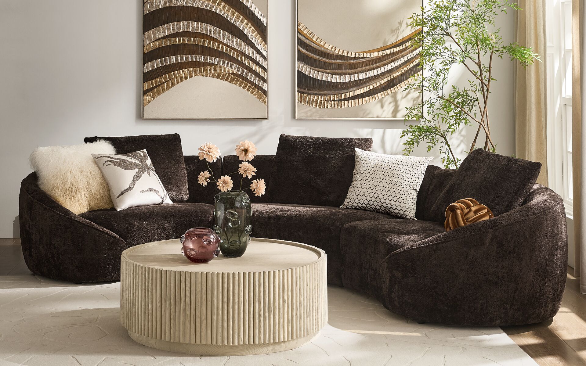 Modern curved charcoal grey boucle sectional sofa paired with a round fluted concrete coffee table and framed textured wall art in an upscale living room.