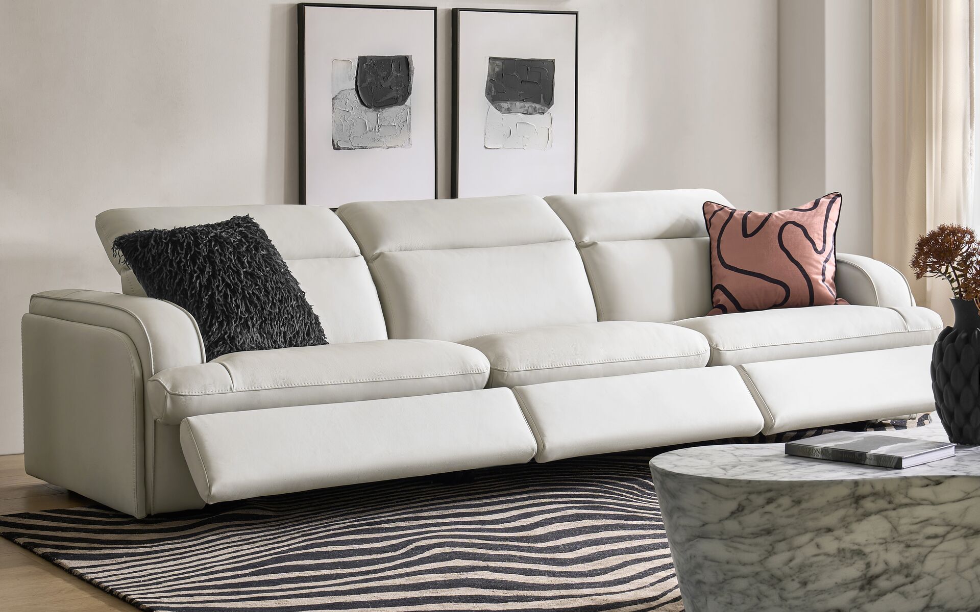 Modern white leather power reclining motion sofa with extended footrests, paired with a marble round coffee table and abstract wall art.