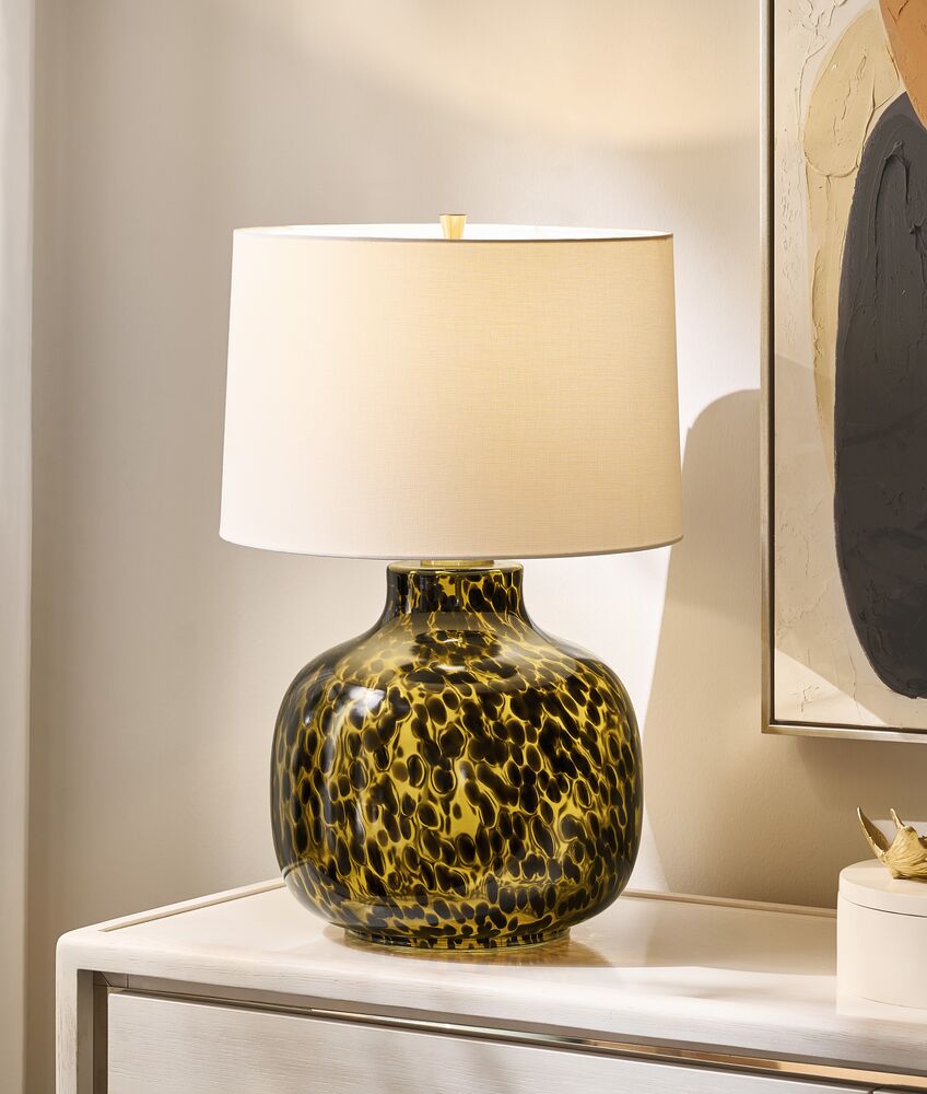 Contemporary table lamp with a tortoiseshell speckled glass base and crisp white fabric drum shade set on a nightstand.
