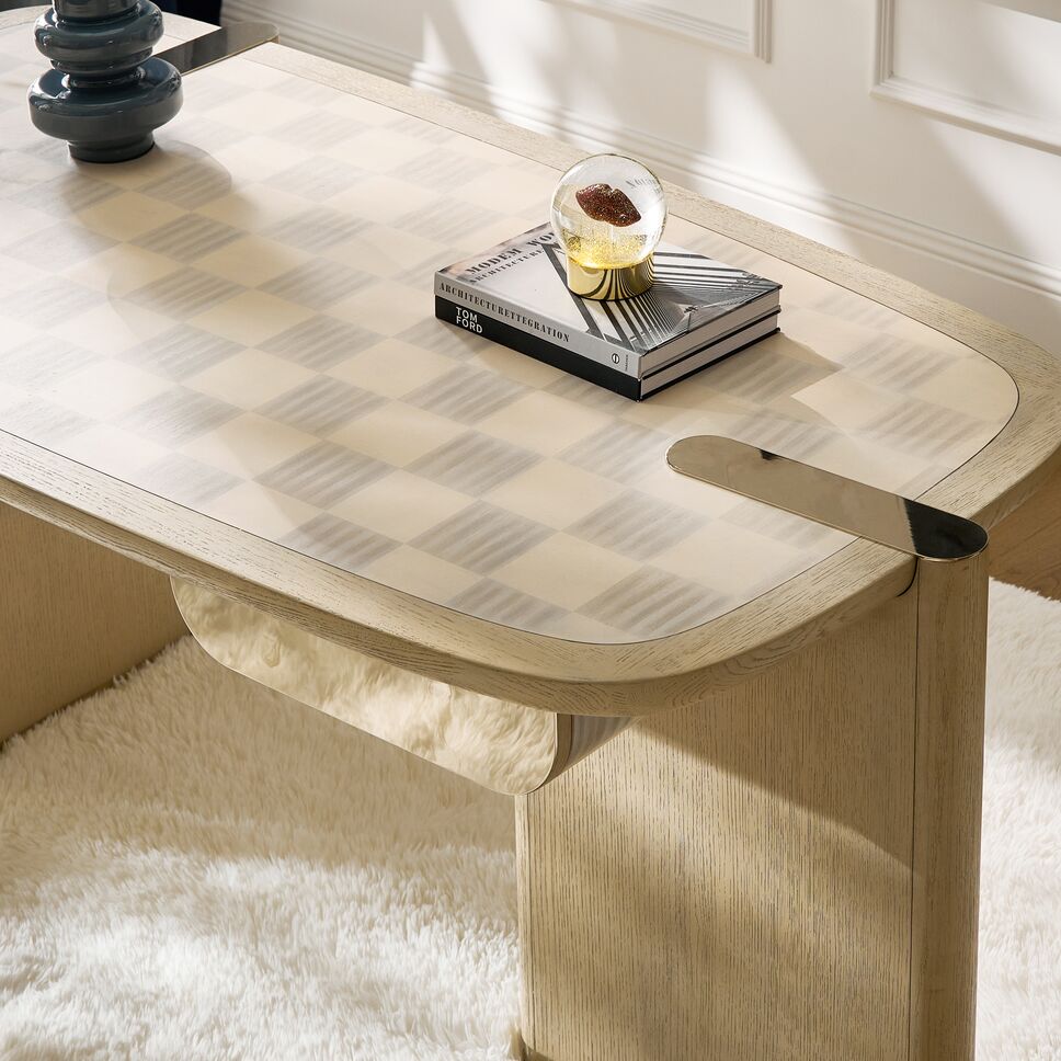 Close-up overhead angle of an oval wood desk highlighting subtle checkered parquet tabletop pattern and brass desktop details.