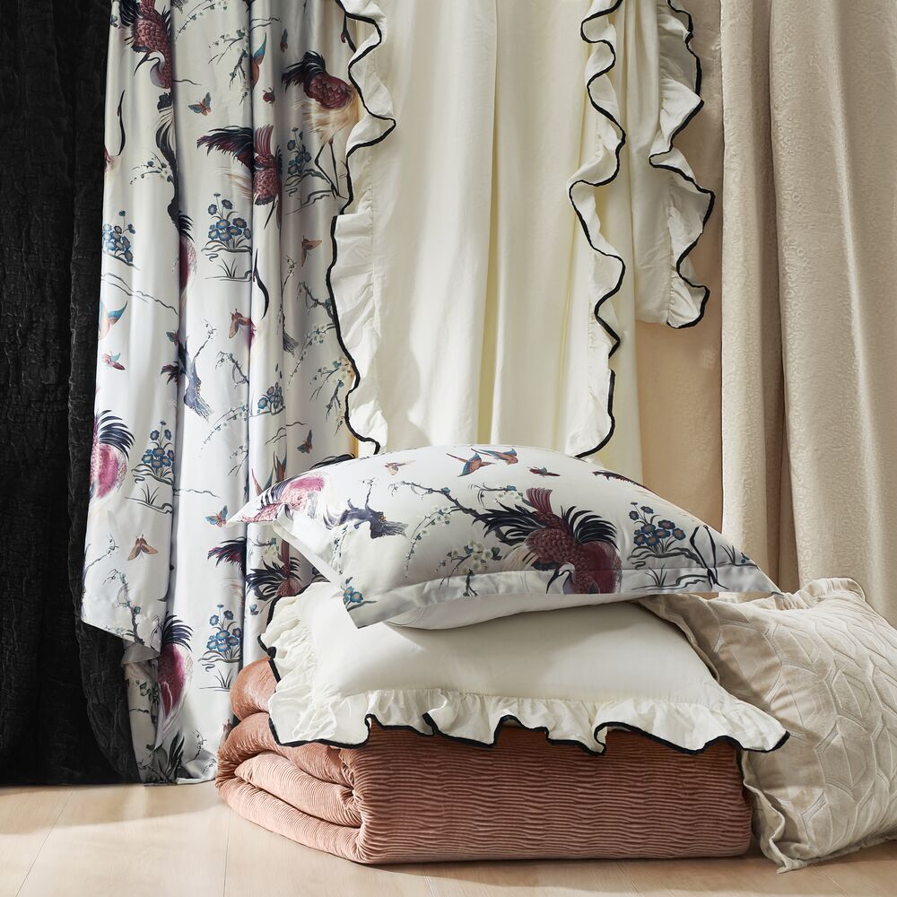 Luxury bedding arrangement showcasing ruffled white pillowcases, floral printed shams, and folded blush quilted blankets.