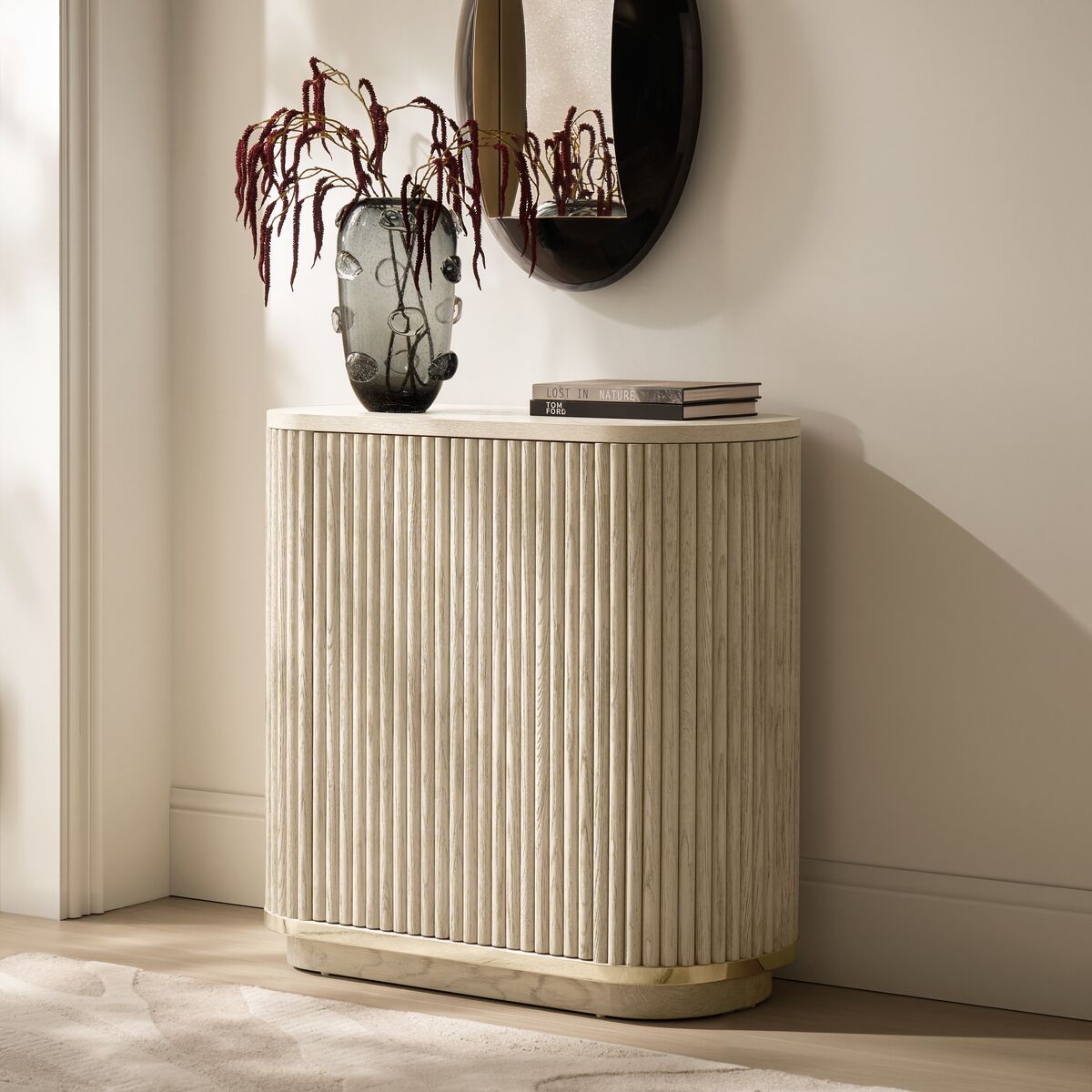 Modern curved fluted light wood accent buffet cabinet with brass plinth base, styled with a textured glass vase and dried floral branches.