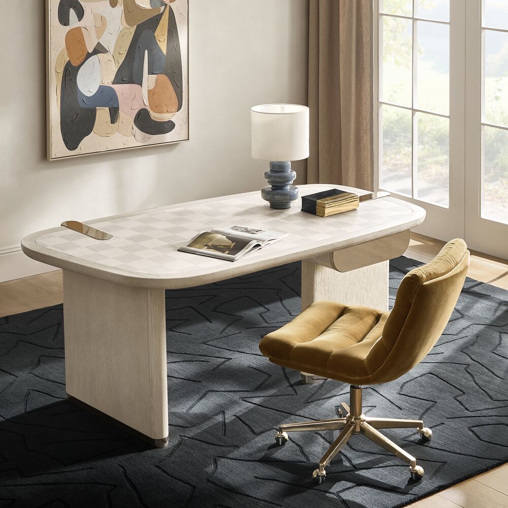 Modern light wood writing desk with subtly patterned top paired with an olive velvet swivel office chair on a geometric dark rug.