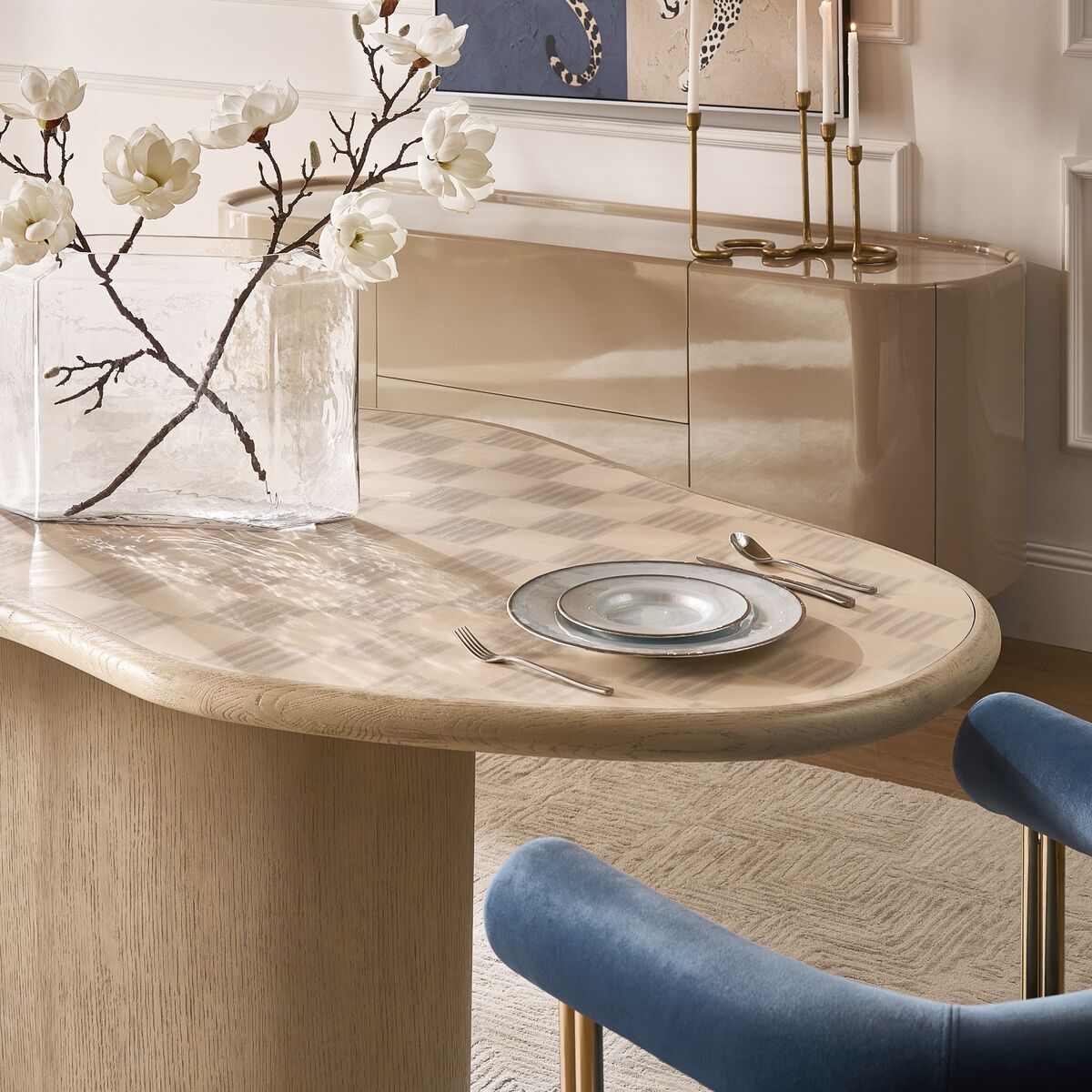 Contemporary oval light wood dining table with elegant place setting, styled with blue barrel dining chairs and buffet sideboard.