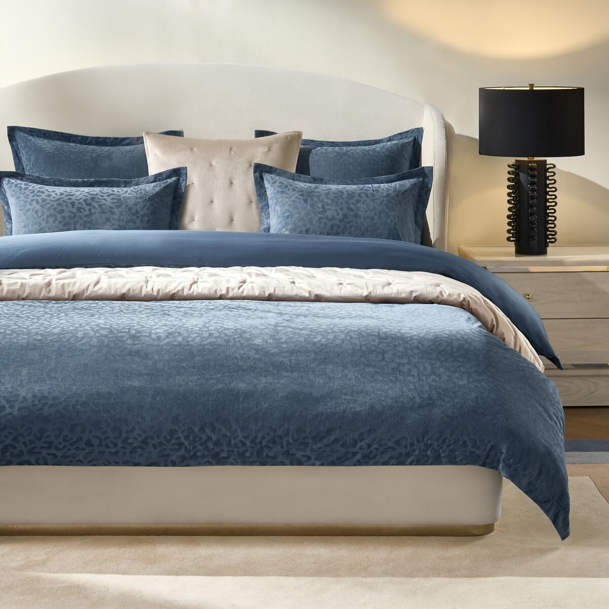 Modern luxury bed dressed in rich deep blue velvet duvet cover with matching euro shams and neutral layered linens.
