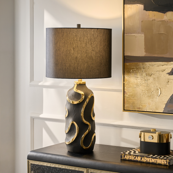 Modern table lamp featuring a black textured ceramic base with gold snake-like squiggles and a black fabric drum shade.