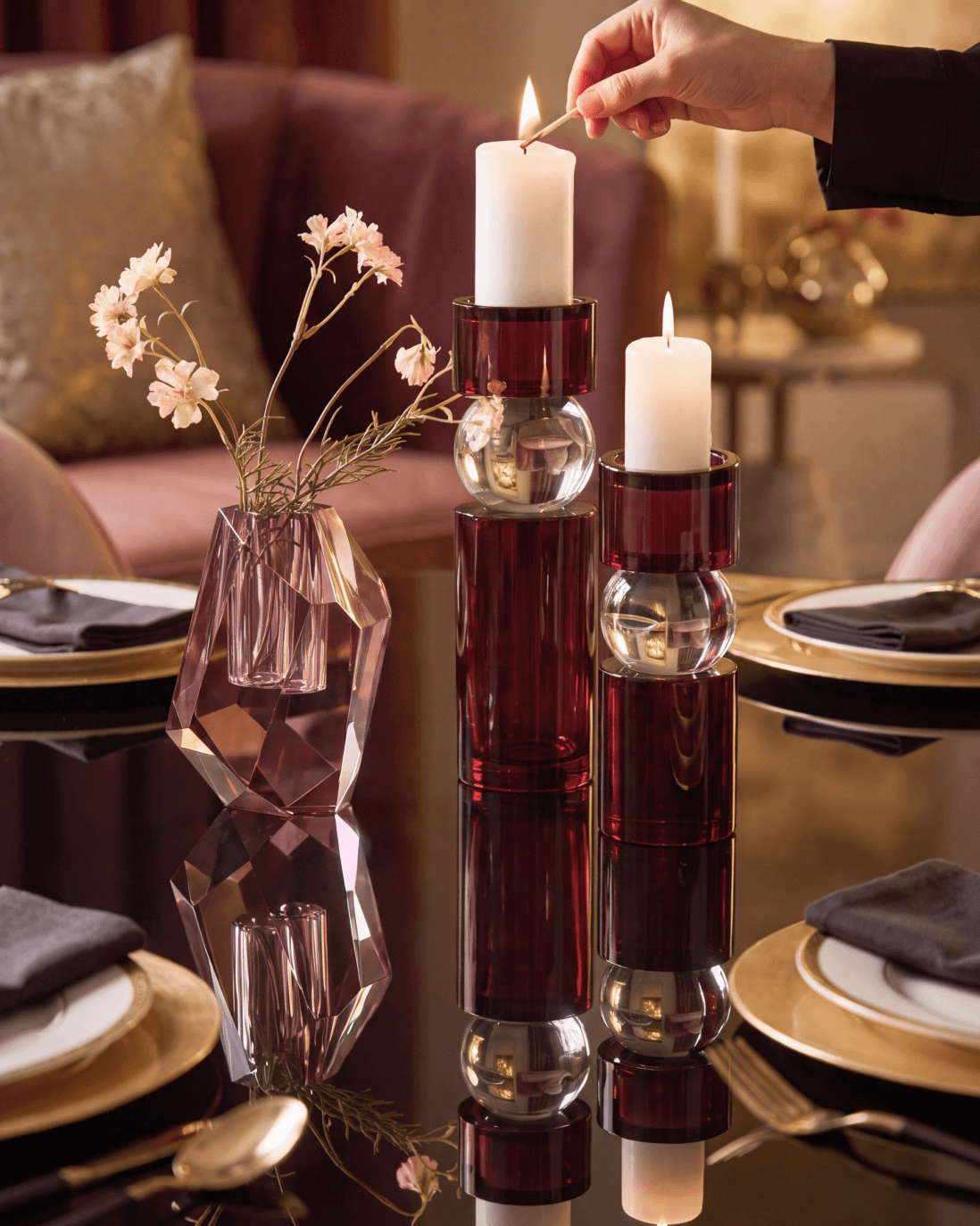 Lighting a white pillar candle set on Leroy Pillar Holders with layered crystal glass and rich fig accents on a reflective dining tabletop.