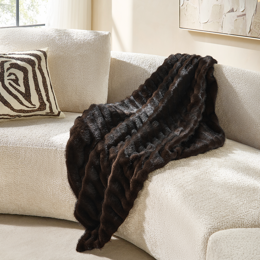 Rich dark brown plush faux fur throw blanket draped softly over the back of a cream boucle curved sofa.