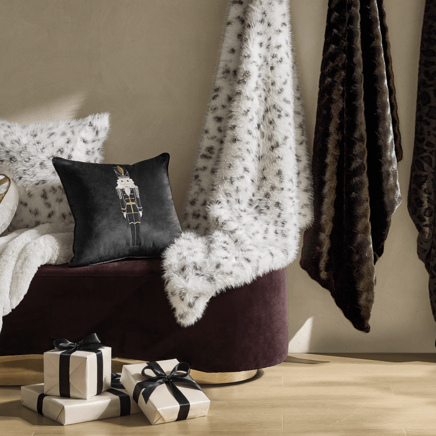 Luxurious faux-fur throw blankets and velvet accent pillows draped over a bench with wrapped holiday gift boxes on the floor.