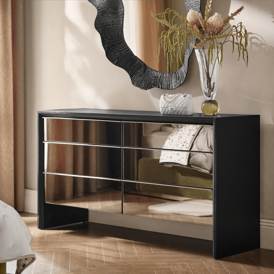 Black double dresser with mirrored drawer fronts styled below a wavy black wall mirror.