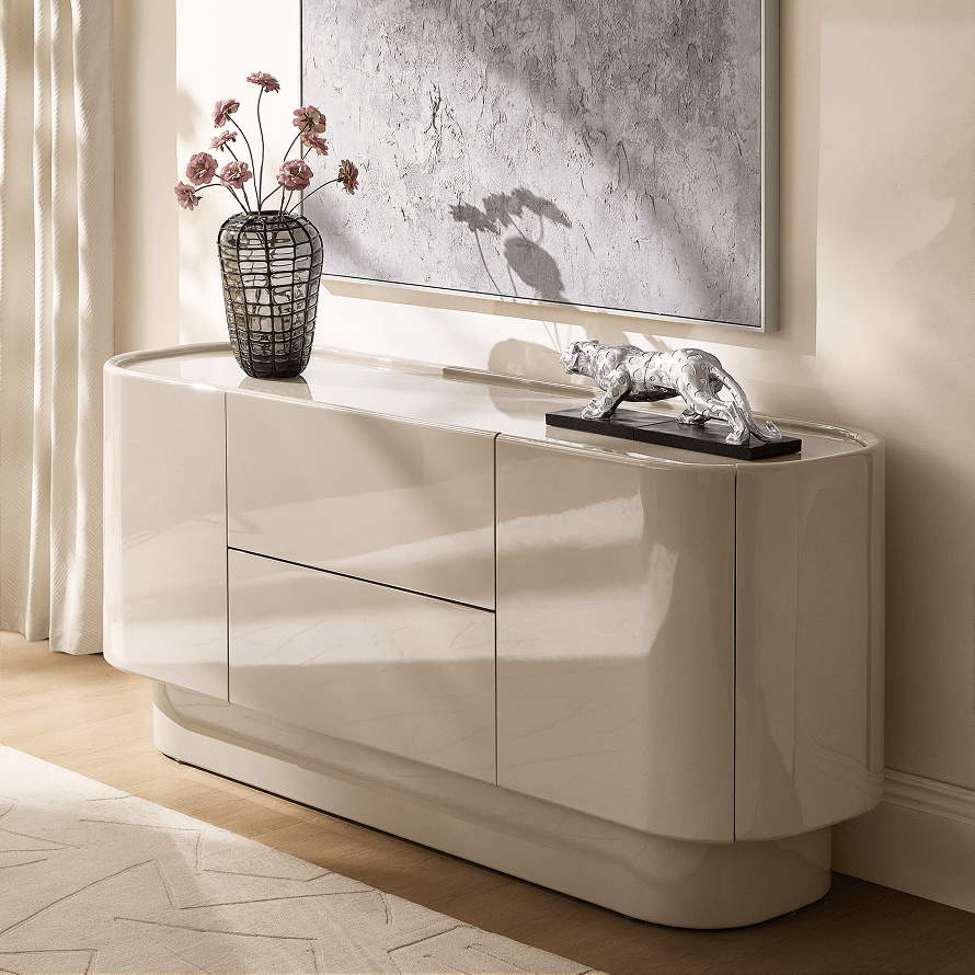 Curved cream high-gloss lacquer credenza styled with a dark textured glass vase, silver leopard sculpture, and canvas wall art.