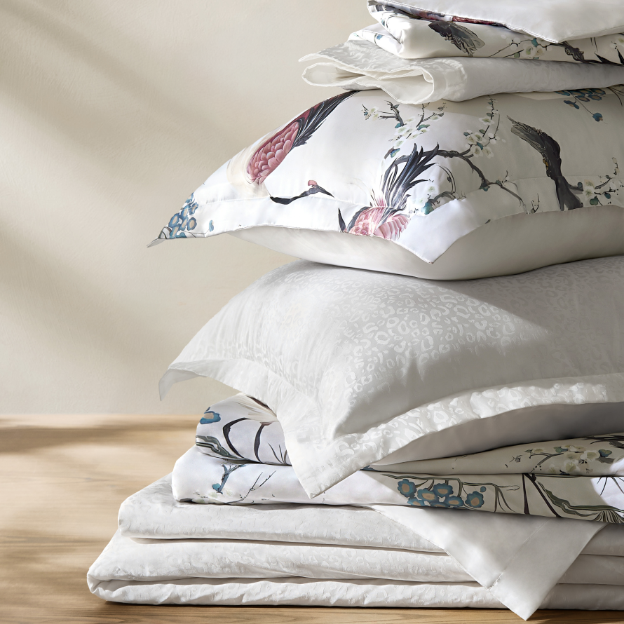 Stack of luxury white bedding featuring an Asian-inspired floral crane print pillow sham and crisp layered sheets.