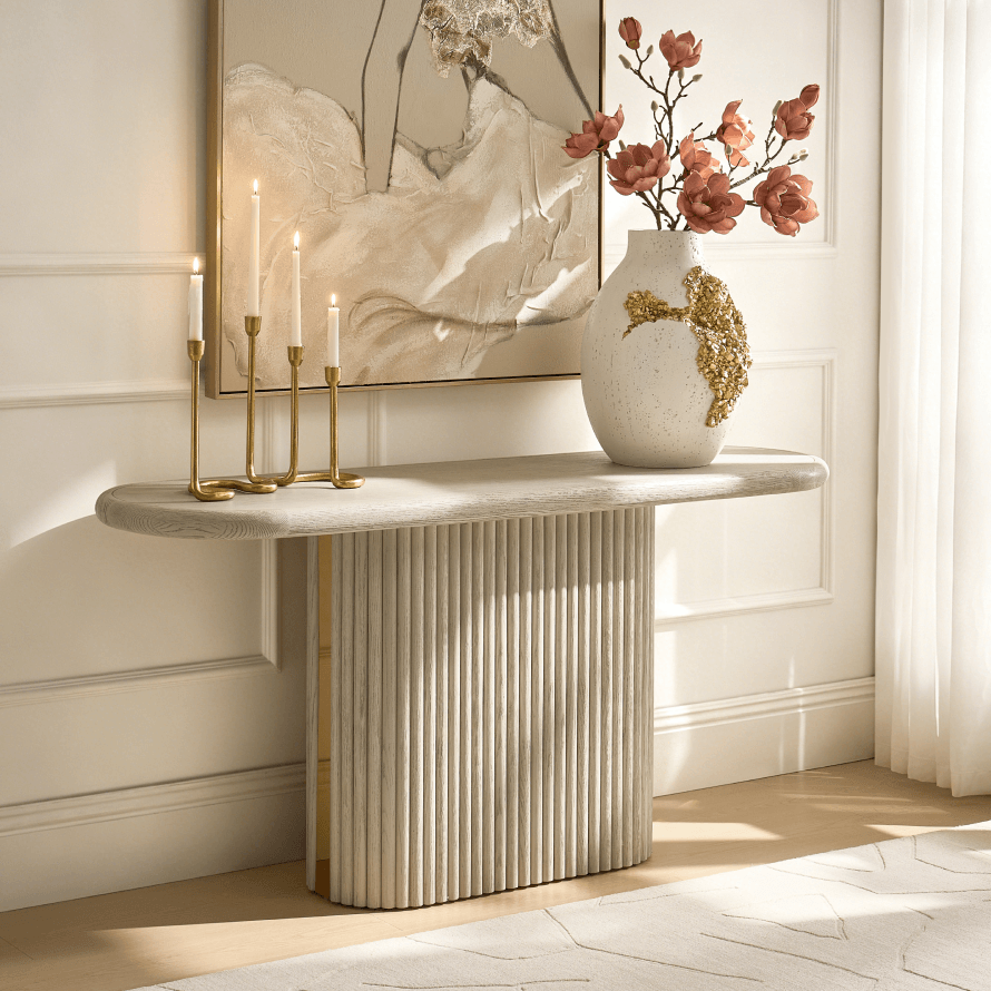 Modern light fluted-base console table styled with tall gold candleholders, a sculptural floral vase, and framed art.