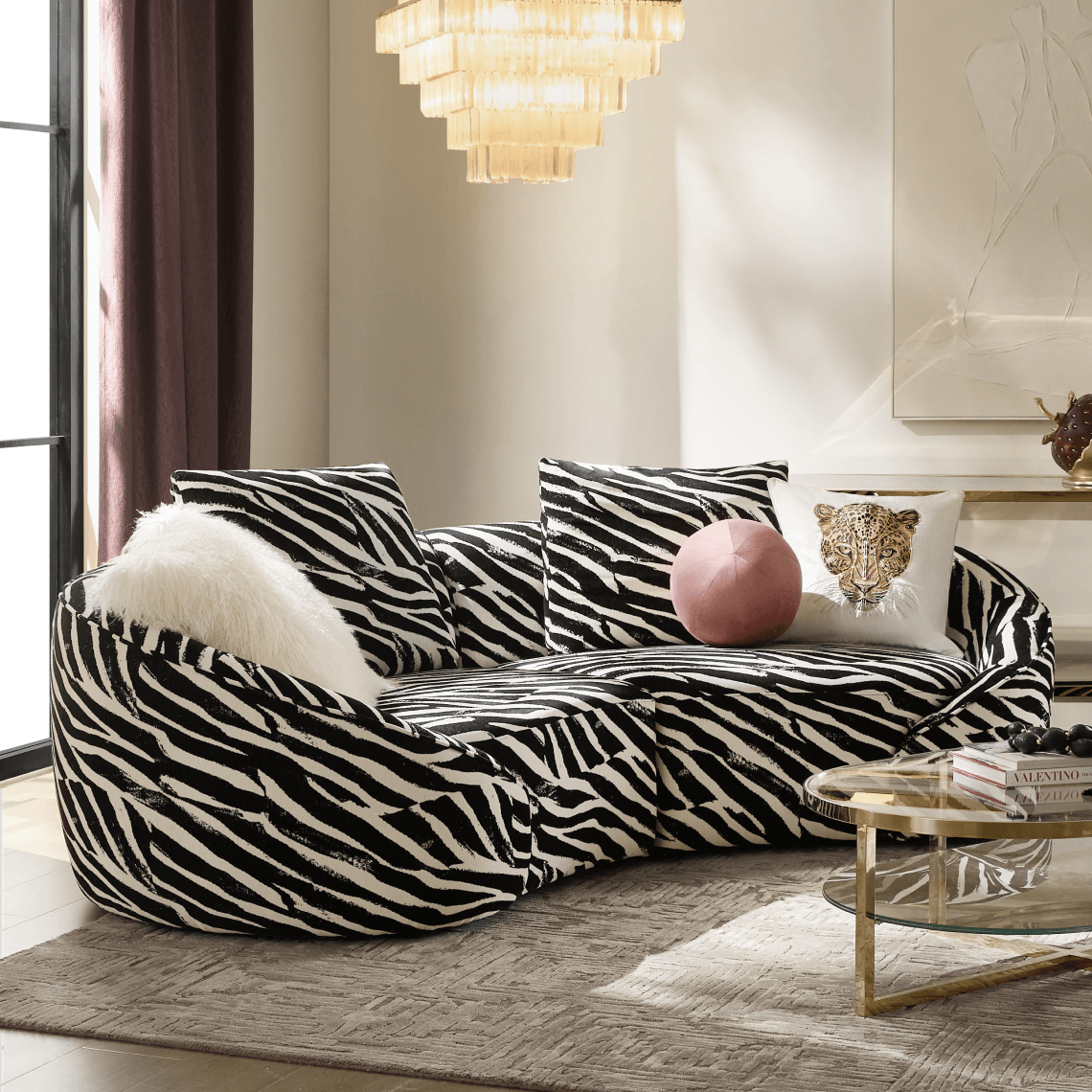 Modern curved sectional sofa in a zebra stripe print, styled with plush accent pillows and a round glass coffee table under a crystal chandelier.