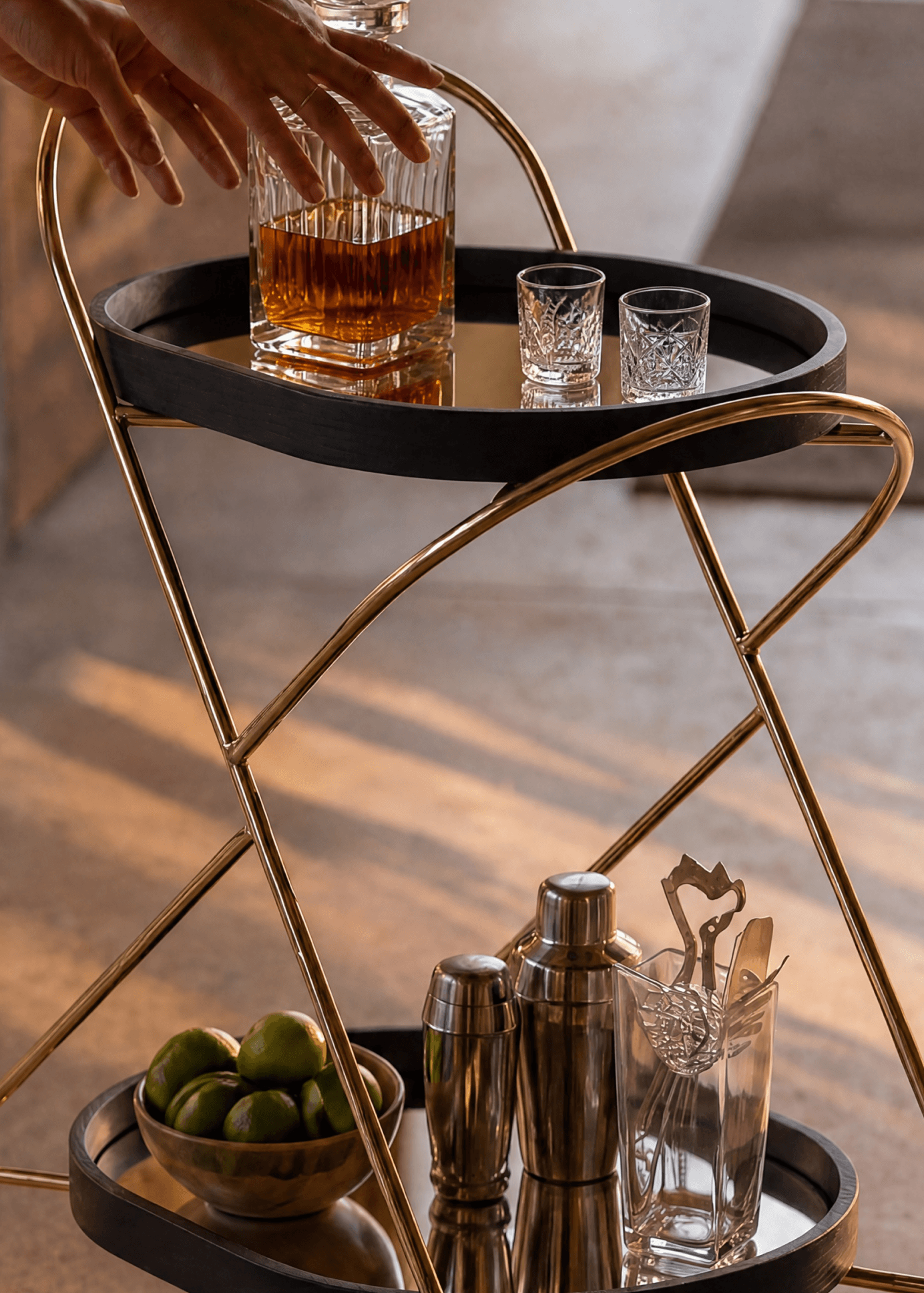 Customer photo of the Cleo Bar Cart featuring a polished brass cross-frame and dark round tiers styled with cocktail glassware and fresh limes at sunset.