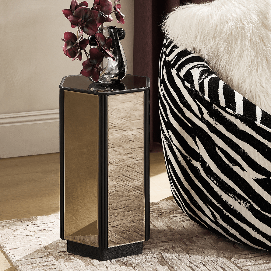 Hexagonal mirrored pedestal side table styled next to a zebra-patterned curved accent chair with a white sheepskin throw.