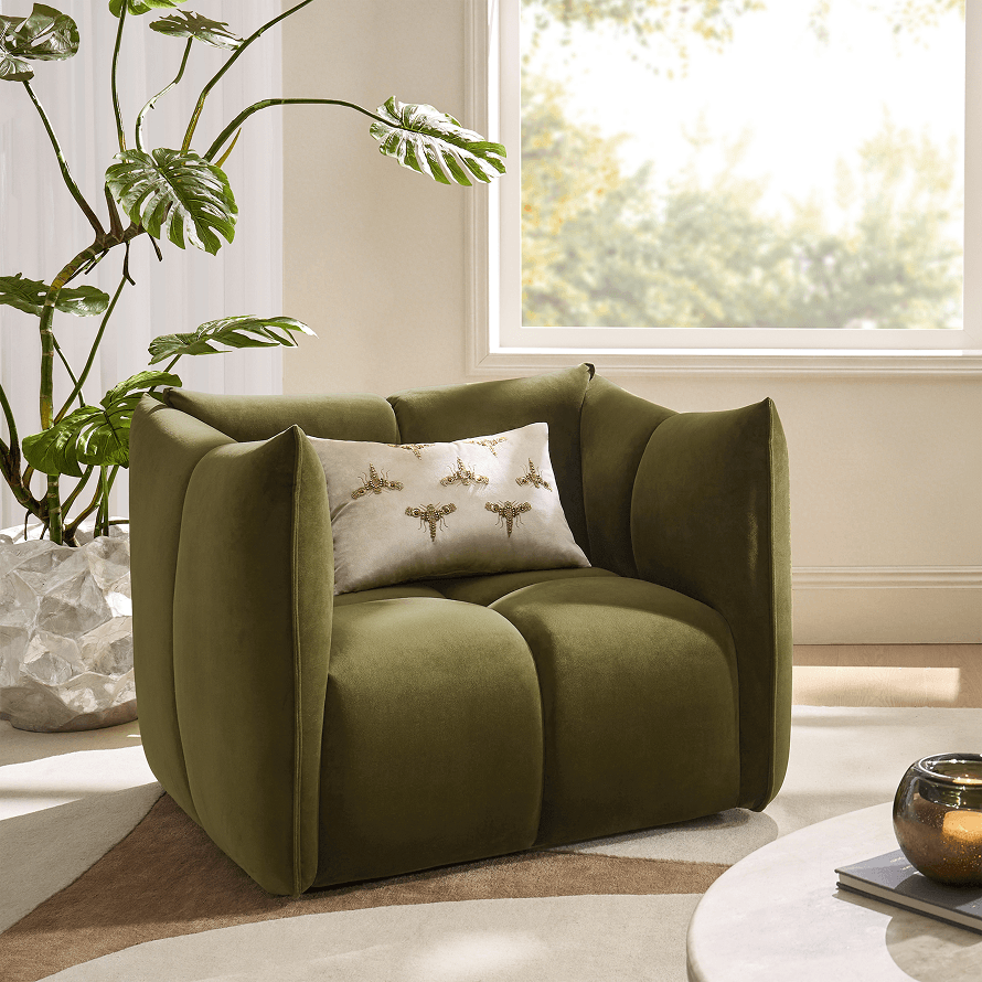 Modern living room corner featuring an olive green velvet armchair with an embroidered bee lumbar pillow near a large window.