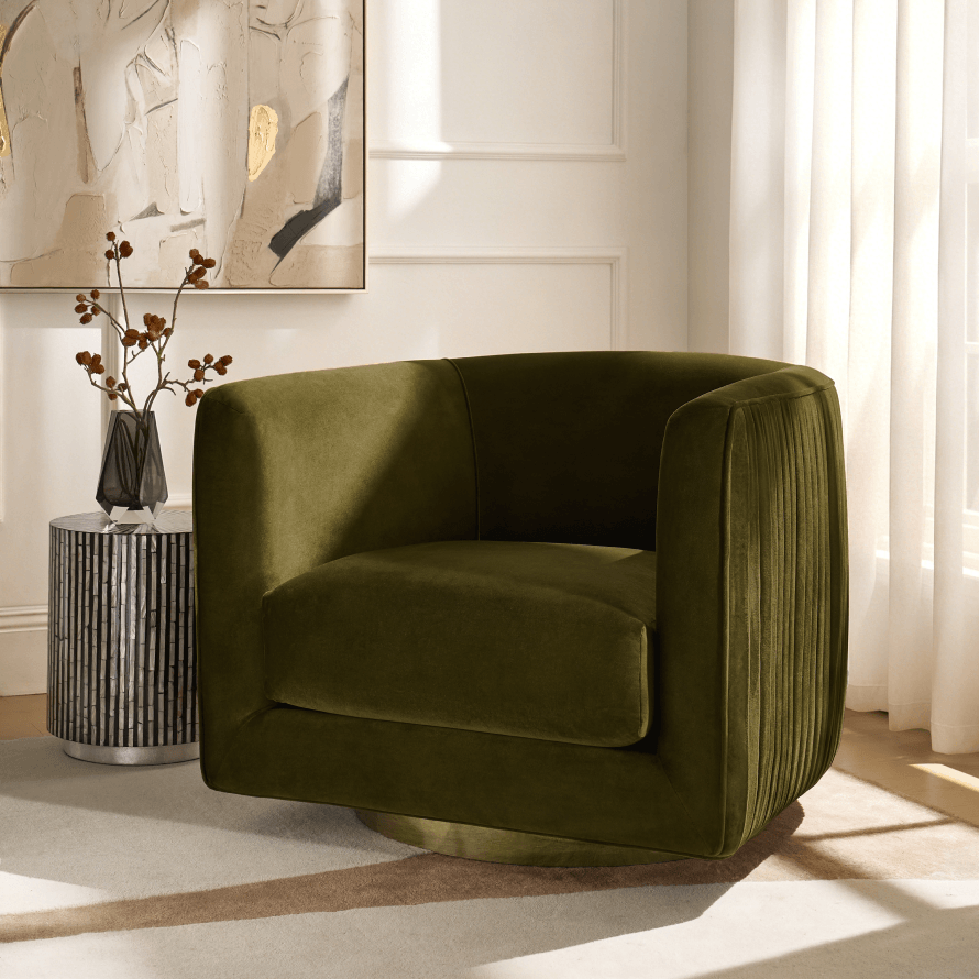 Luxurious olive green velvet swivel barrel chair with a pleated back and gold base styled against a white wall with wall art.