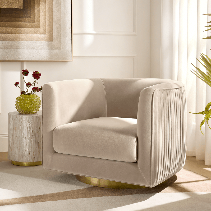 Modern cream velvet swivel barrel chair with subtle pleated exterior detailing and a gold plinth base beside a small marble side table.