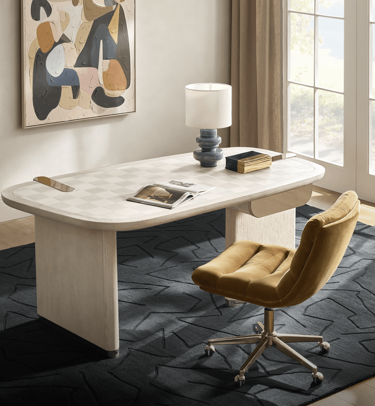Modern luxury home office with an oval light wood desk featuring a checkered inlay top, ochre velvet swivel chair, tiered blue ceramic lamp, and geometric area rug beneath abstract canvas art.