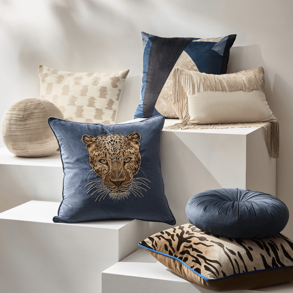 Layered collection of luxury decorative pillows featuring a blue embroidered tiger motif, tiger stripes, and neutral textured cushions.