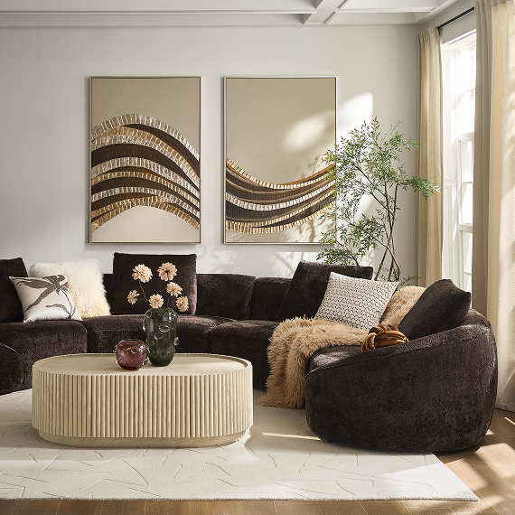 Elegantly styled living room with a dark brown sectional sofa, fluted oval coffee table, and large textured wall art pieces.