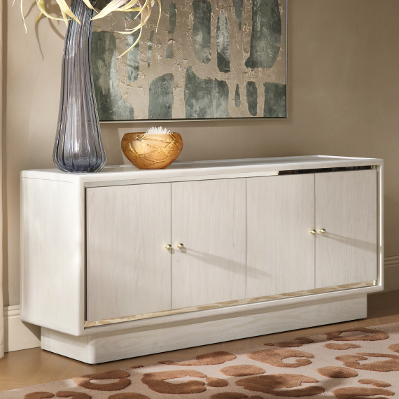Contemporary white four-door buffet cabinet with brass trim detail, styled with a tall fluted glass vase on a leopard print area rug.