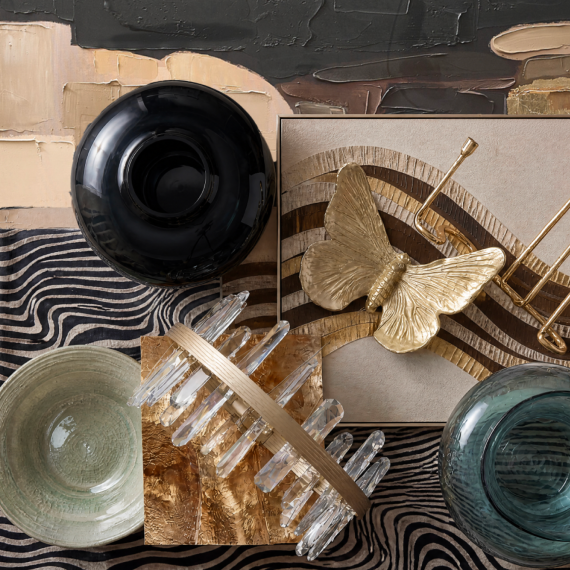 Flat lay composition of design mood board materials including a butterfly accent piece, crystal sconce fixture, ceramic bowl, and zebra pattern fabric.