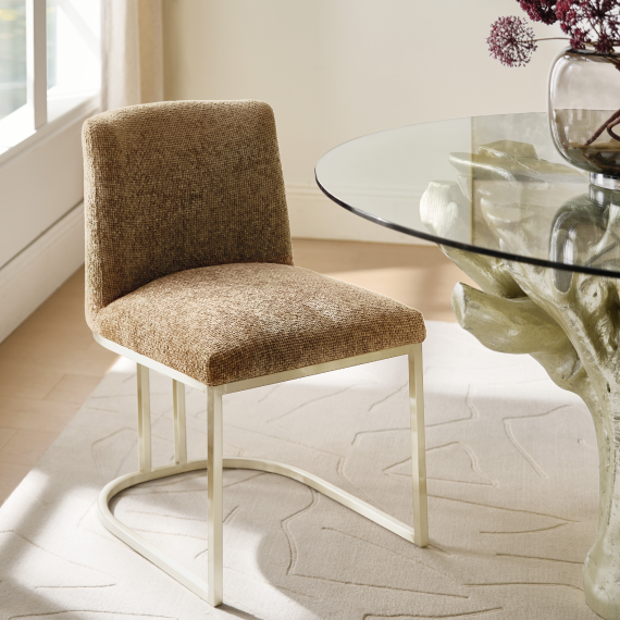 Textured brown fabric dining chair with a brass sled base frame positioned next to a glass top dining table.