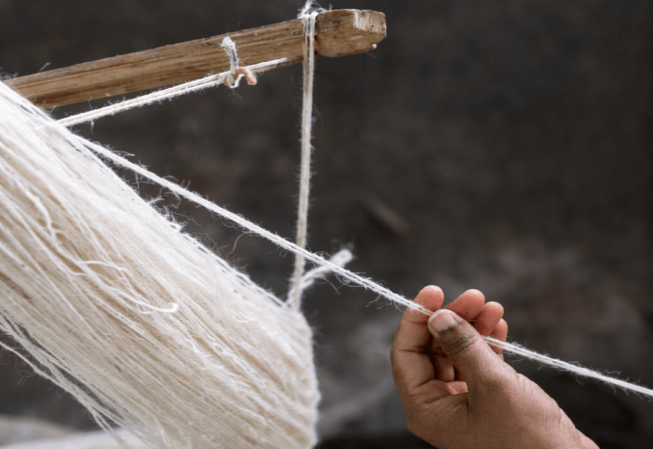 Close-up of an artisan hand-spinning raw natural wool yarn using traditional spinning tools.