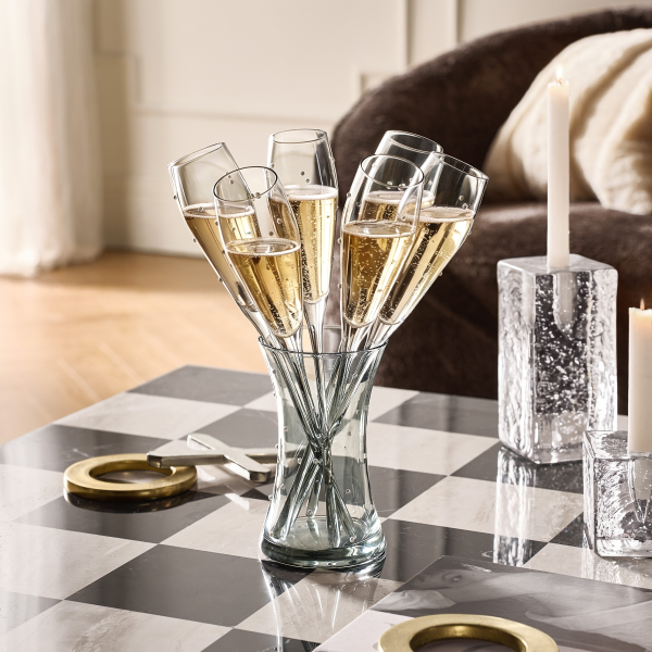 Array of crystal champagne flutes arranged in a glass holder on a checkered coffee table with brass accents.