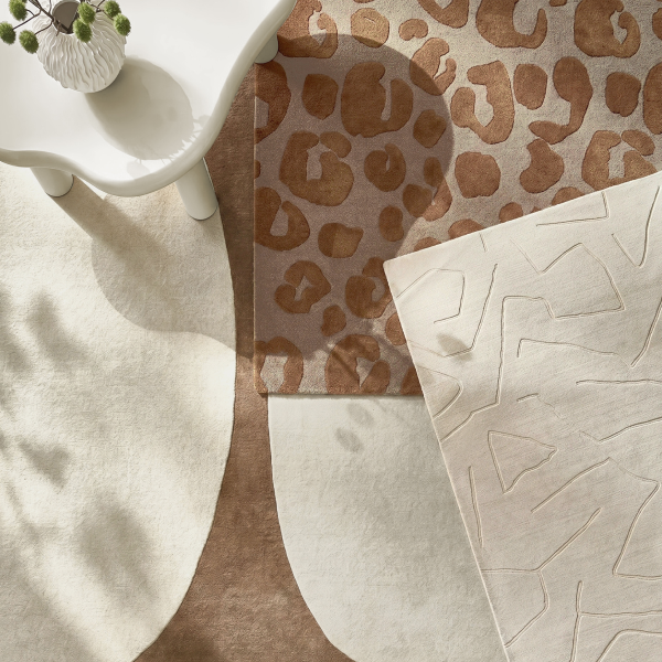 Top-down view of layered modern area rugs featuring cream wool and leopard animal print textures near a side table.