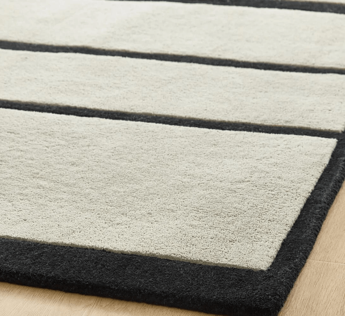 Close-up corner of a plush wool rug showing tailored ivory panels bordered by sharp contrast black lines.